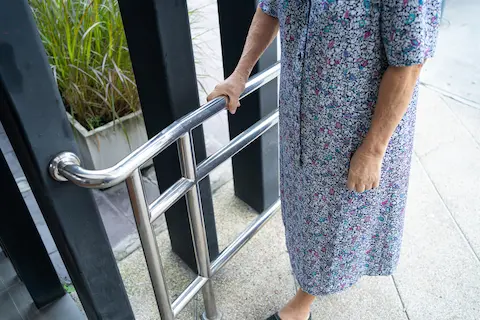 Elderly woman using a safety handrail for support, showcasing the importance of home modification for senior accessibility and fall prevention by Thrive @ Home Network.