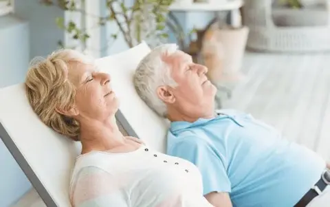 White senior couple laying side by side on patio loungers napping - thrive at Home Network