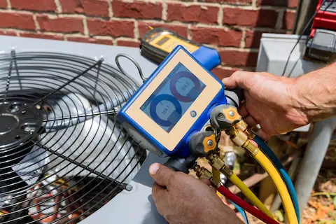 Man holding equipment near air conditioning unit.